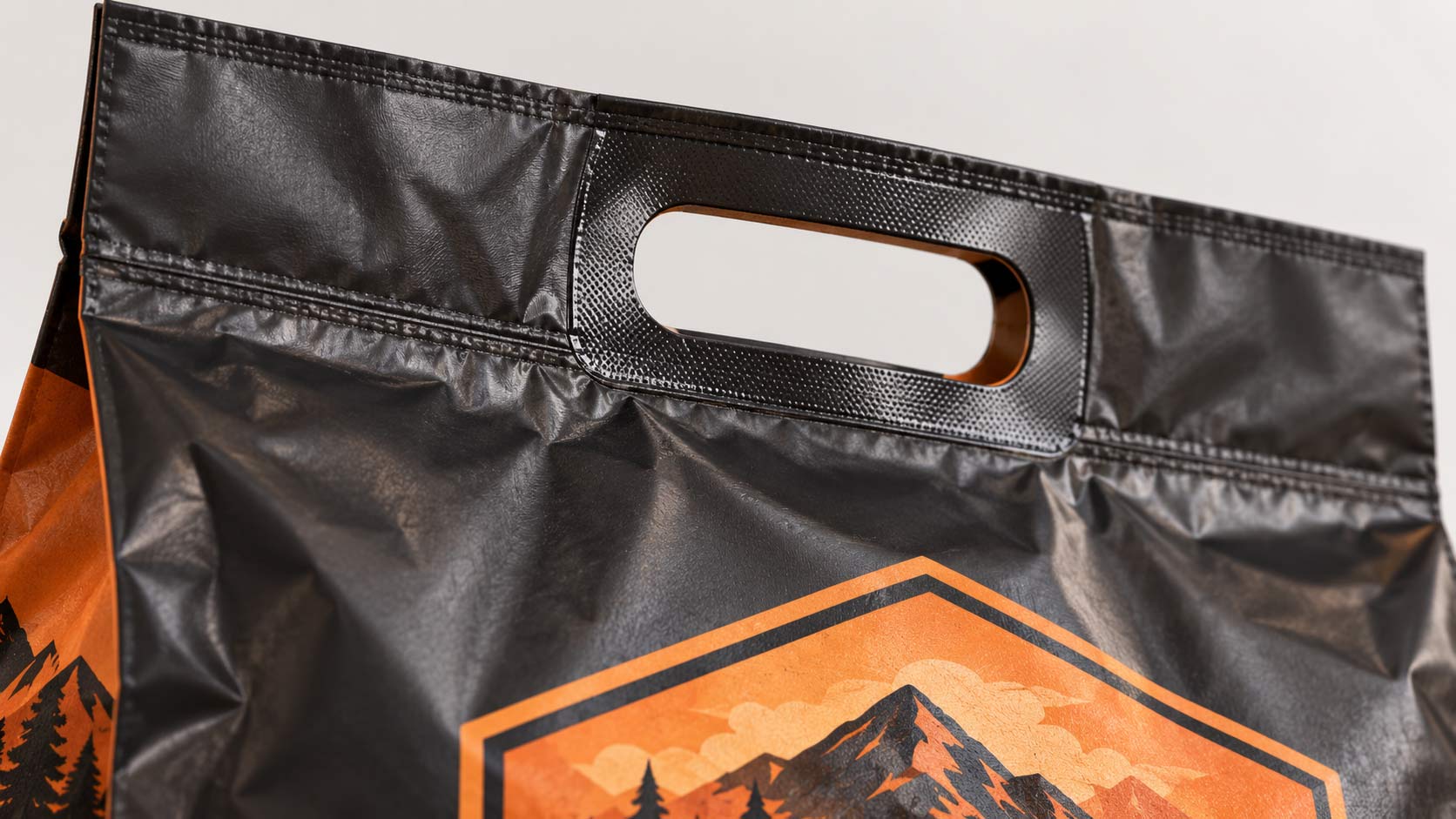 Close-up of a die-cut handle on a large kibble bag showing the reinforced patch laminated behind the cut opening, positioned above the sealed chamber
